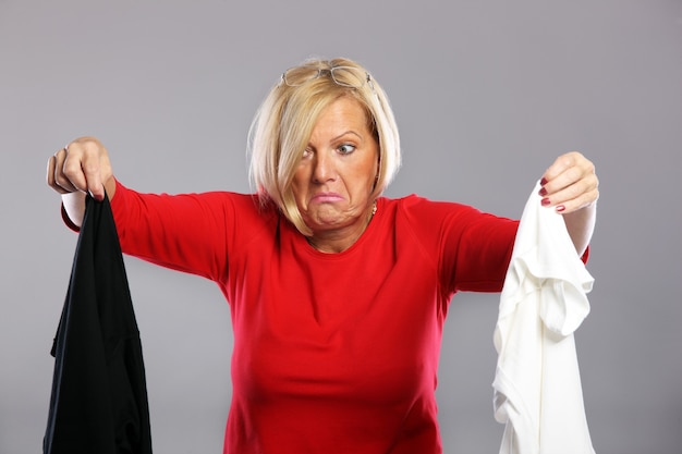 Photo a mature woman holding dirty clothes over grey