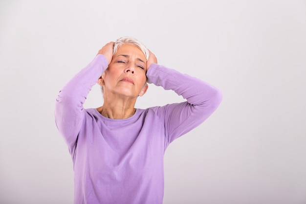 Mature woman holding her head with her hands while having a headache and feeling unwell. Senior woman with headache, pain face expression.