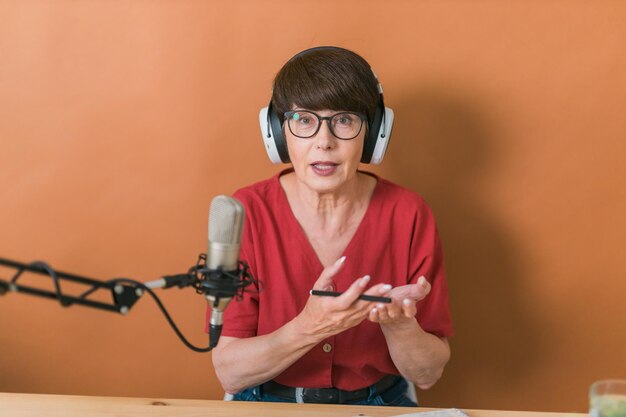 Mature woman making podcast recording for her online show Attractive business woman using headphones front of microphone for a radio broadcast