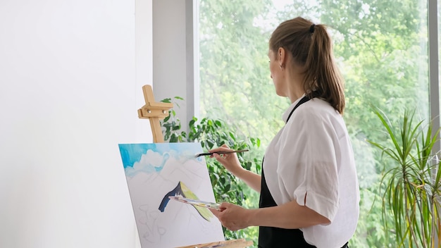 Mature woman paints sky on canvas with paintbrush closeup