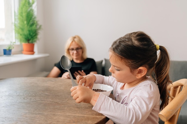 Mature woman reading tablet or ebook while preschool girl eating alone Social media addiction