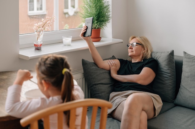 Mature woman reading tablet or ebook while preschool girl eating alone Social media addiction