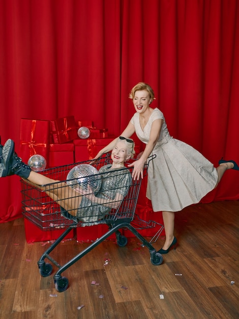 Mature woman rolling stylish senior woman in sunglasses and silver dress the supermarket cart