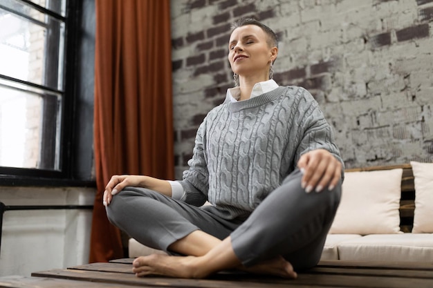 Mature woman sitting at home on table in yoga pose relaxing