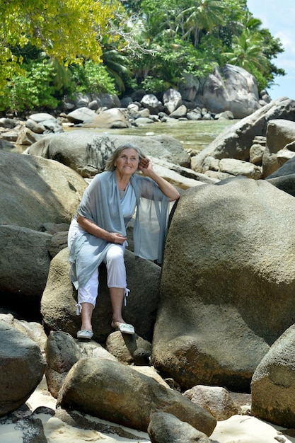 Mature woman sitting at sandy beach with rocks