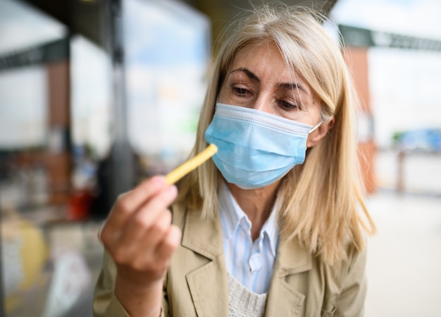 Mature woman trying to eat a french fry wearing a mask, funny coronavirus concept