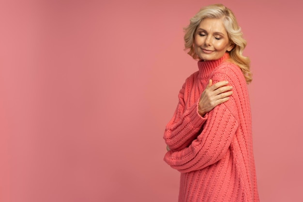 Mature woman wearing stylish winter sweater isolated on pink background. Shopping concept