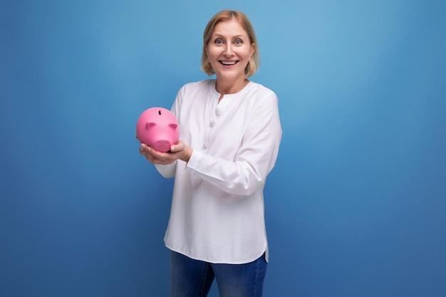 Mature woman with blond hair holds savings in a piggy bank