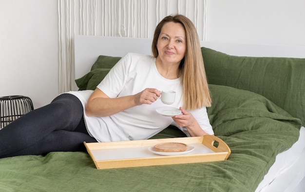 Mature woman with coffee mug sitting on edge of bed portrait