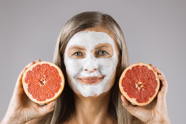 Mature woman with face mask holding slices of grapefruit