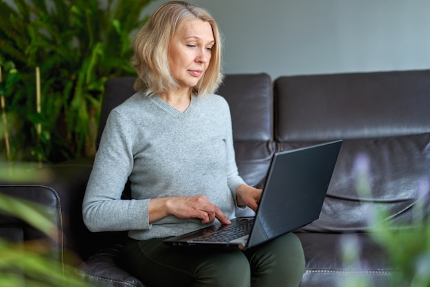 Mature woman working online sitting on a sofa in an home