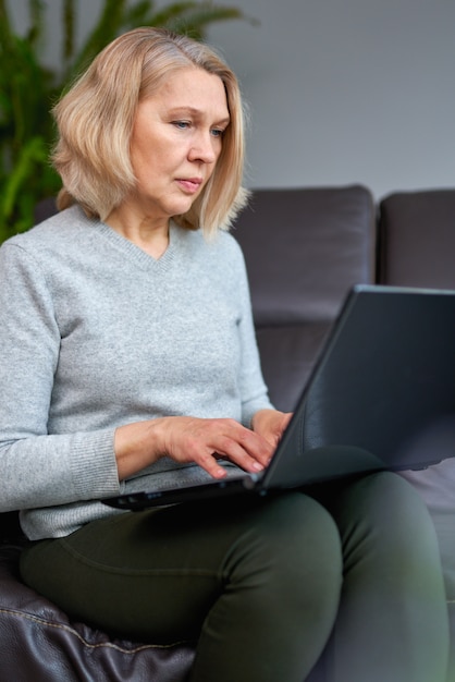 Mature woman working online sitting on a sofa in an office.