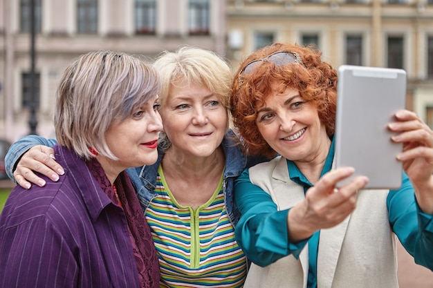 Mature women are taking photos by tablet PC outside.