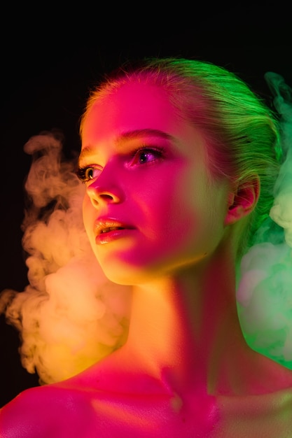 Mavelous. Portrait of female fashion model in neon light on dark studio background with smoke. Beautiful caucasian woman with trendy make-up and well-kept skin. Vivid style, beauty concept. Close up.