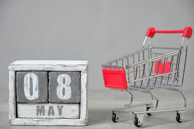 May 08 shopping cart and wooden calendar gray backgroundConcept for Fair Trade Day