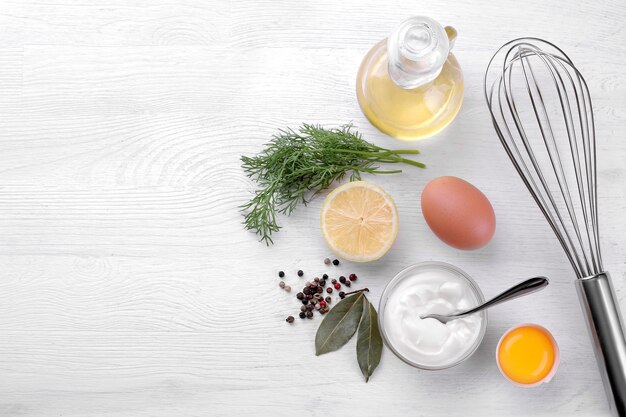 Mayonnaise in a glass bowl and ingredients for making mayonnaise on a white wooden background. white sauce. with space for text