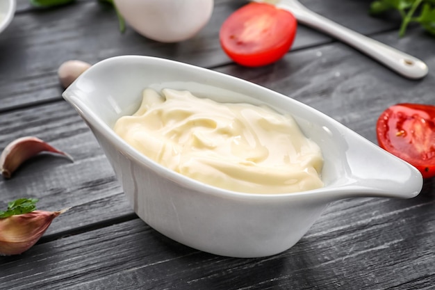 Mayonnaise in gravy boat with ingredients on wooden background closeup