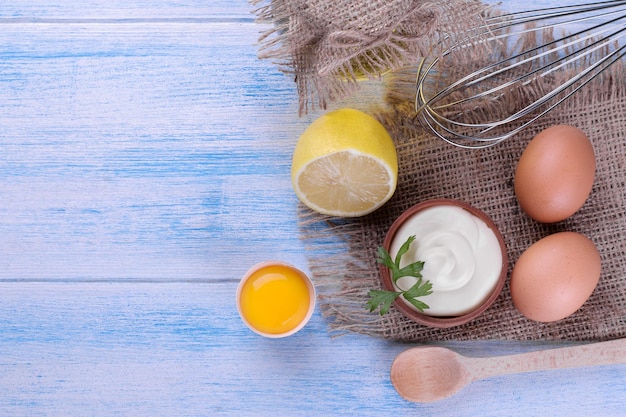 Mayonnaise in a wooden bowl and ingredients for making mayonnaise on a blue wooden background white sauce top view with space for text