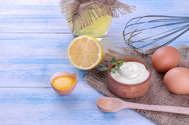 Mayonnaise in a wooden bowl and ingredients for making mayonnaise on a blue wooden background. white sauce.