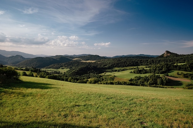 meadows with green grass, mountains, blue sky with clouds and sun landscape