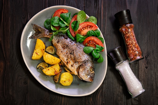 Meal.Baked Dorado fish with vegetables in the oven on a dark background.