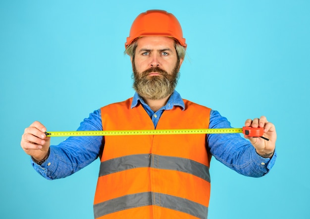 Measuring concept. bearded man in hardhat. brutal hipster worker use tape measure. Man in uniform works on production. Industrial modern technology. builder with tape. Yellow colored measuring tape.