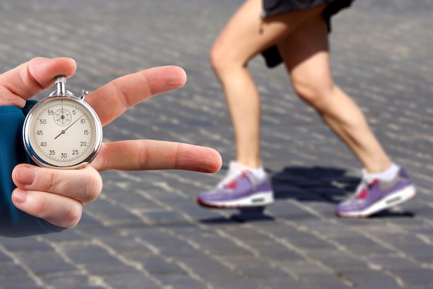 Measuring the running speed of an athlete using a mechanical stopwatch hand with a stopwatch on the background of the legs of a runner