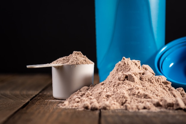 Measuring scoop of whey protein on wooden table to prepare a milkshake. 