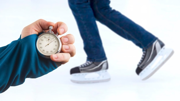 Measuring speed on skates with a stopwatch hand with a stopwatch on the background of the legs of a man skating on an ice rink