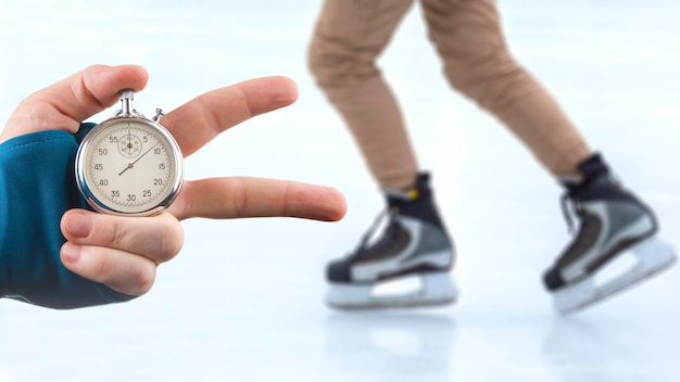 measuring speed on skates with a stopwatch. hand with a stopwatch on the background of the legs of a man skating on an ice rink