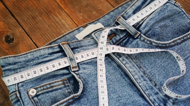 Measuring tape and jeans on a wooden background. Slimming concept