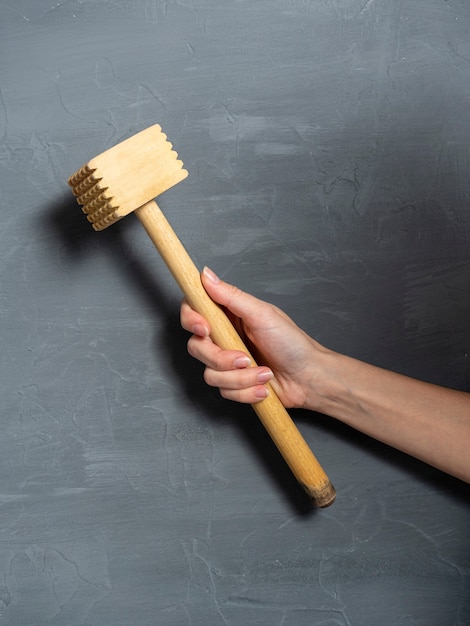 Meat beater in a woman's hand on a gray textured background. Kitchen tools, vertical photo