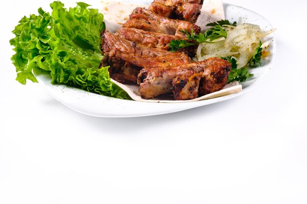 Meat kebab on ribs on lavash with onions and cabbage on a white plate on an isolated white background