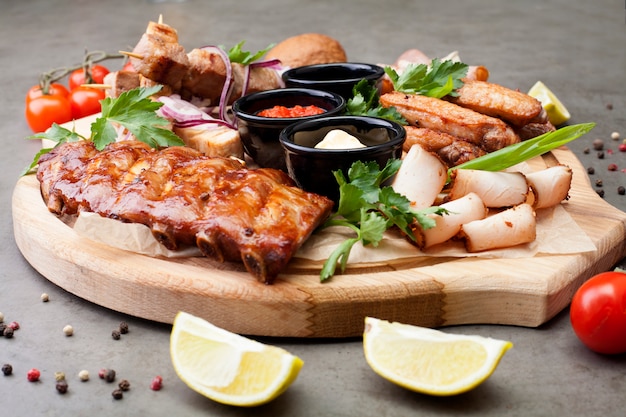 The meat plate is filled with cuts and steaks, decorated with herbs, cherry tomatoes and lemons. The concept of meat or beer appetizer.