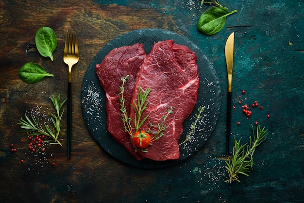 Meat. Raw veal steak with rosemary and spices. On a black stone background. Top view.