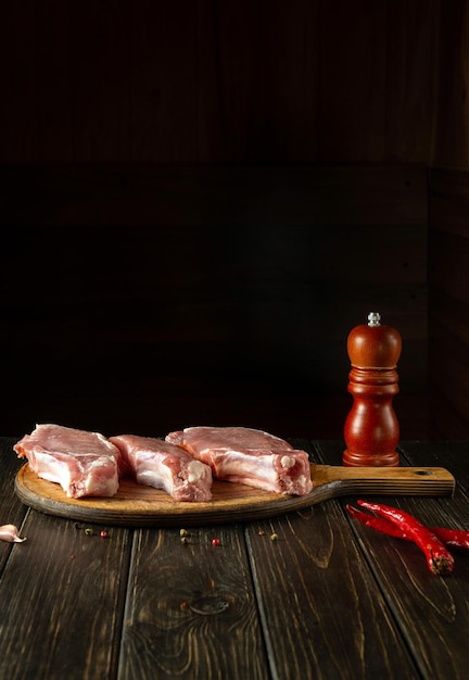 Meat sliced raw rib steaks on a kitchen cutting board before cooking with spices and peppers Dark space for menu or recipe