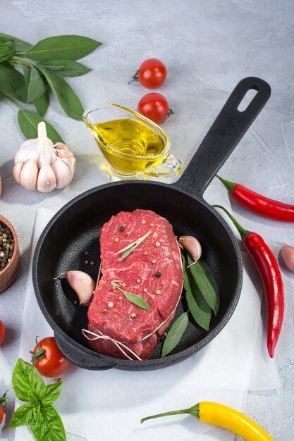 Meat steak on frying pan with ingredients for cooking on a gray concrete background Top view. Copy space.