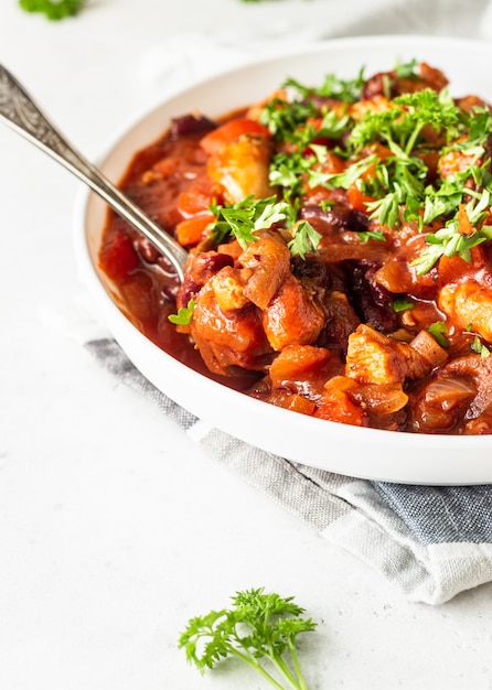 Meat stew with red beans, bell pepper and onion in tomato sauce in a white plate over light grey slate 