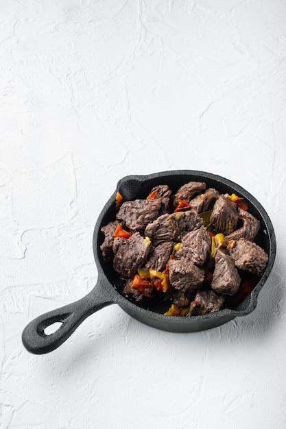 Meat stew with sweet bell pepper and bay leaf in cast iron frying pan on white stone surface with copy space for text