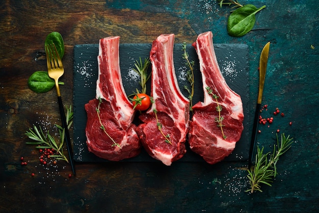 Meat Three raw veal steaks on the bone with rosemary and spices On a black stone background Top view