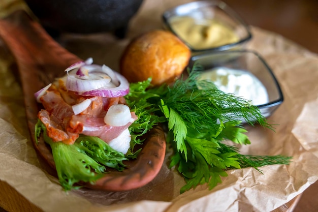 Meat on a wooden spoon plate served with herbs and sauces