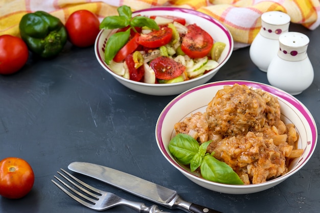 Meatballs in sour cream sauce and fresh vegetable salad in bowls