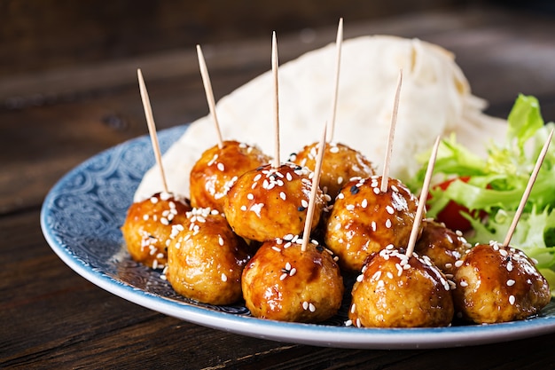 Meatballs in sweet and sour glaze on a plate with pita bread and vegetables in a Moroccan style on a wooden table.