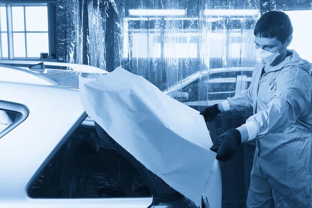 Mechanic covering car with paper before painting in auto repair service