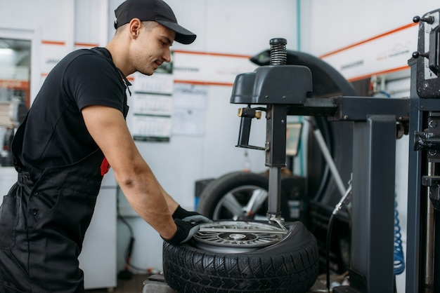 Photo mechanic fixing broken wheel on tire fitting machine, repairing service. man repairs car tyre in garage, automobile inspection in workshop