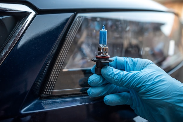 Mechanic hold car halogen light bulb for repair against headlight car in background