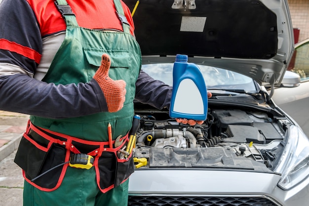 Mechanic holding bottles with oil near car engine