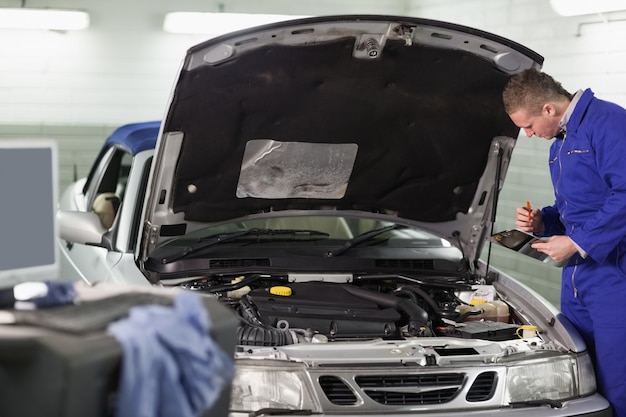 Mechanic holding a clipboard while looking at the engine