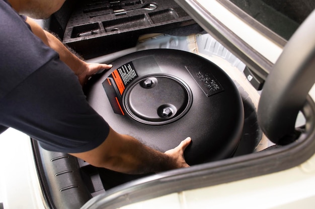 A mechanic is installing a car donutshaped LPG tank in a spare wheel hole in a auto repair garage