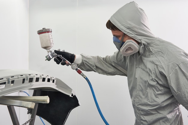 Mechanic painting bumper of a car with sprayer in painting booth in repair auto service